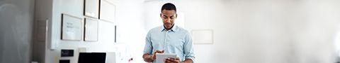 Person in a small office standing and looking at a smart tablet in their hands.