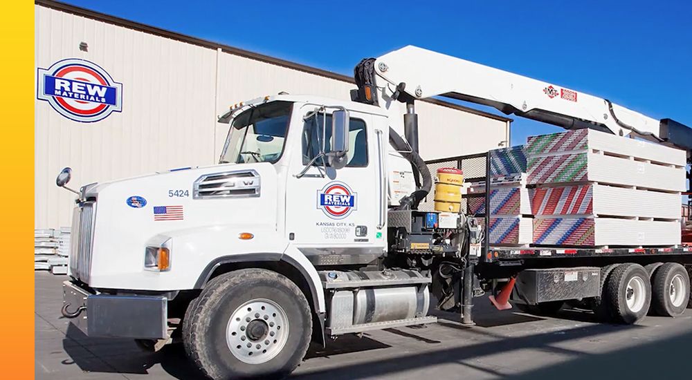 Rew Materials tractor trailer truck ready to deliver pallets of sheetrock from its crane lift 