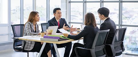 Four office professionals sitting in modern conference room across from each other discussing the day’s business.