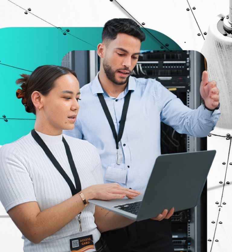 Two IT specialists reviewing information on a laptop held by one while standing in front of computer server rack.