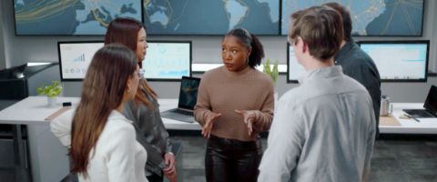 Four businesspeople discuss something in front of computer screens 