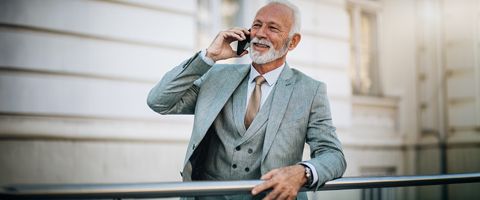 A man in a gray suit talks on the phone while leaning against a railing