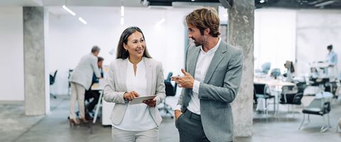 A man and a woman in business attire smile and talk in a modern office space