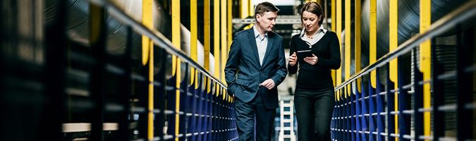 Businessman and woman walking down a hall while looking at a tablet device