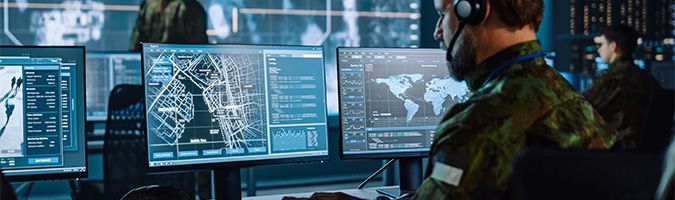 Military man working on multiple desktop monitors with a headset on