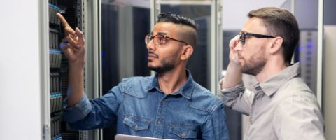 Two people standing in a server room point and look at equipment