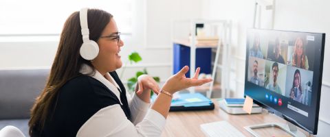 Person in business attire sitting in a home office and talking in a video call on a desktop computer.