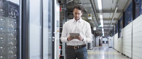A person walks through a data center while looking at the tablet in their hands.