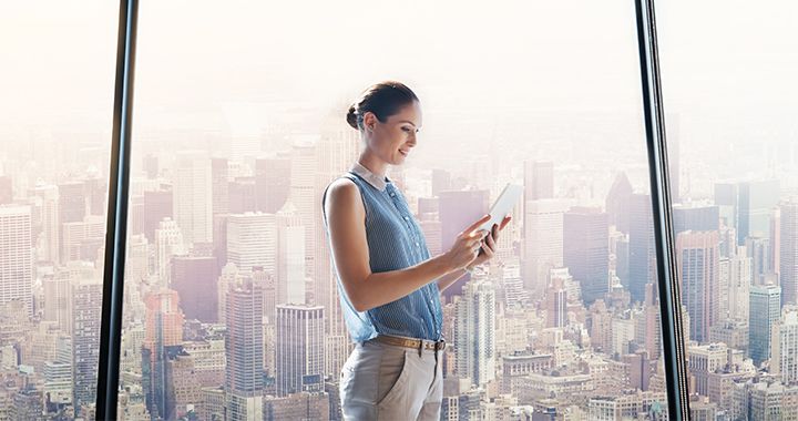 Woman standing in front of a large window overlooking the city while looking at a tablet