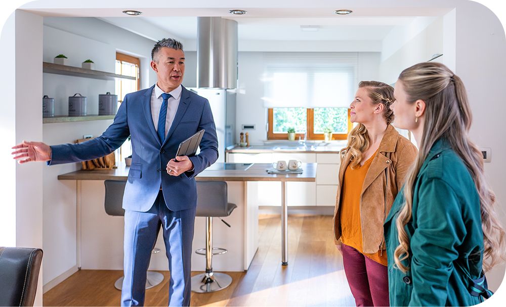 Relator standing in home kitchen area holding computer tablet discussing the home with two clients. 