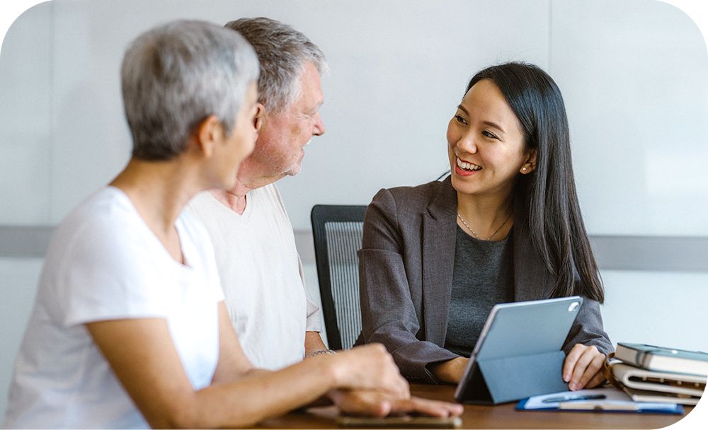 Relator sitting at desk showing two clients data on computer tablet. 