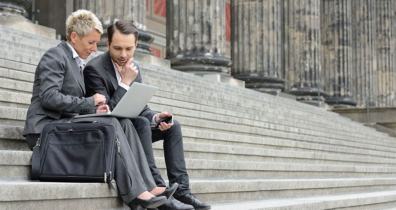 Two business people sitting on stone steps while working on a laptop device