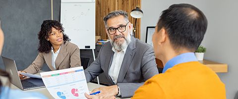 Business man and woman in suits sitting at table while talking to another person sitting across from them.