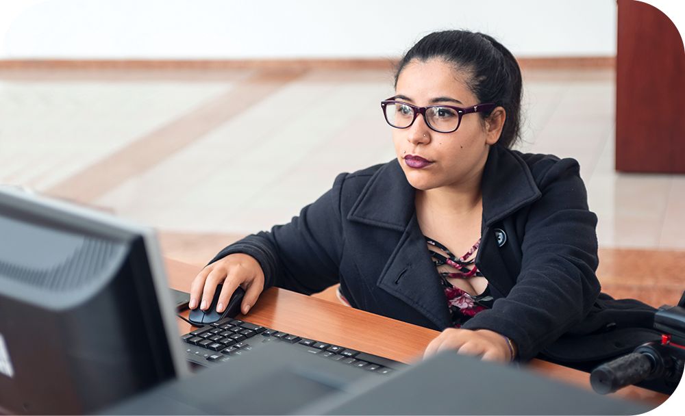 Woman in a black jacket sitting at a desk while working on a desktop computer