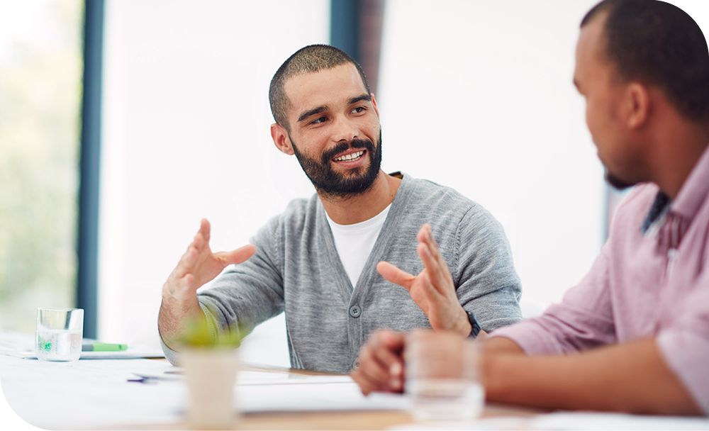 Man in a gray sweater sitting and talking to a person sitting across from him