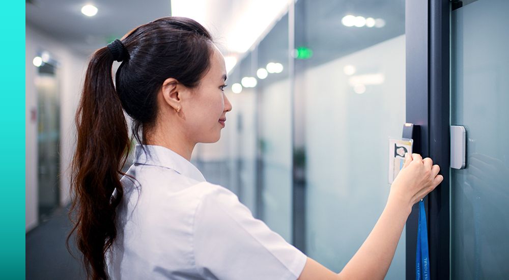 Woman in a white shirt standing in front of a door while using an ID card to unlock it