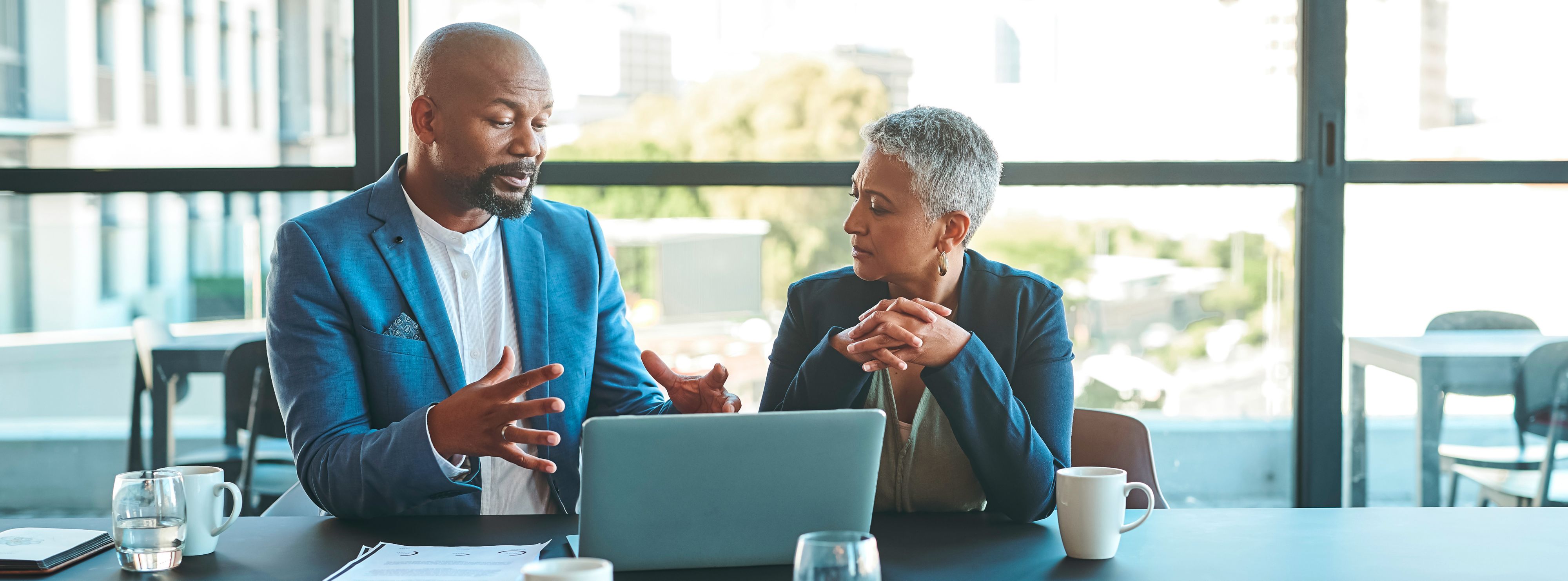 Two coworkers discuss their work in front of an open laptop.