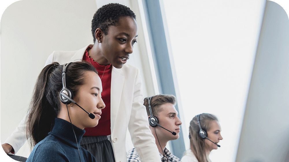 Three people with headsets sit and work while a woman stands between two of them