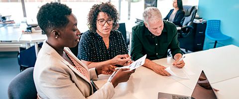 Three businesspeople collaborate on a document together at a table in an office setting