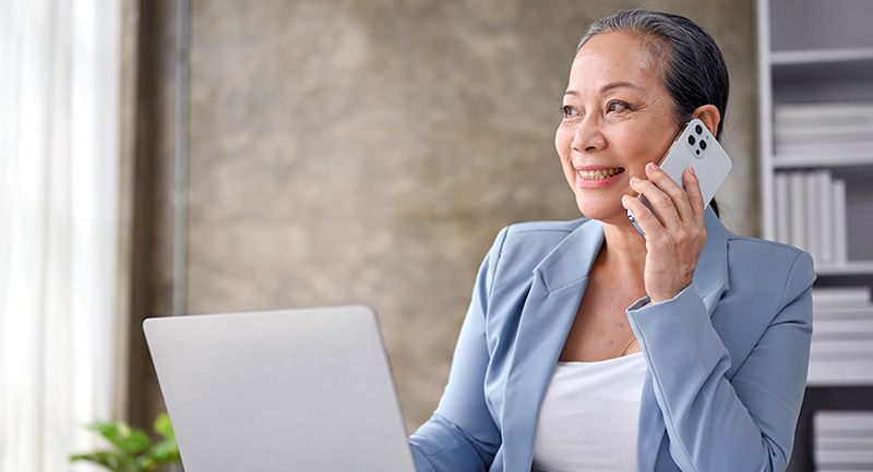 A woman in a suit talks on the phone in front of a laptop
