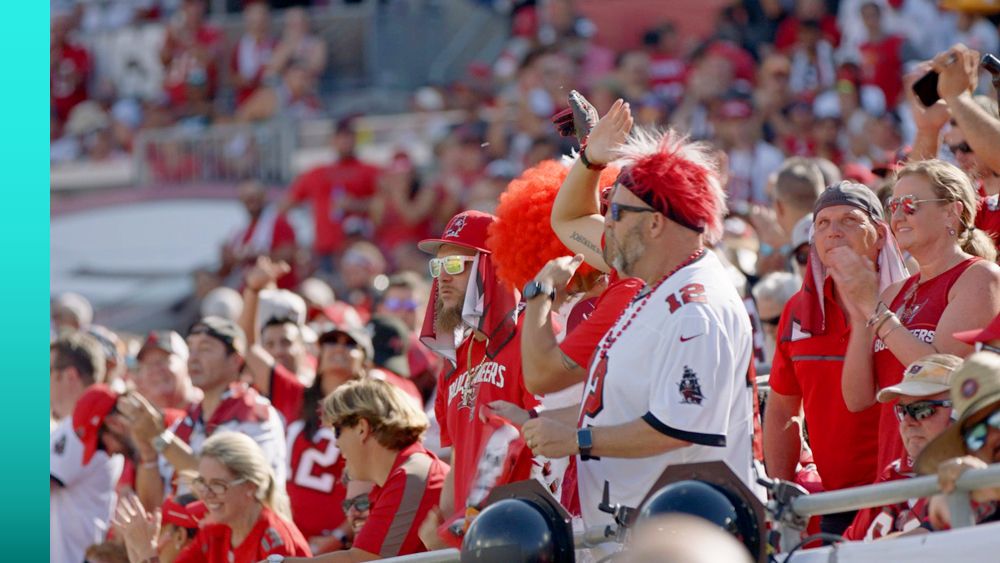 Fans cheer at Raymond James Stadium wearing Buccaneers’ colors and gear.
