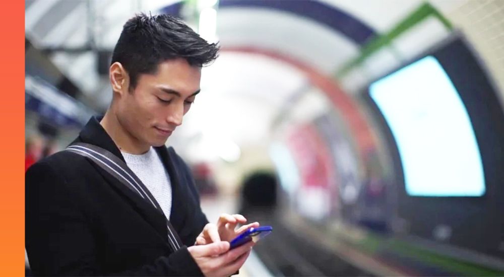 A person looking at a smartphone while standing on a train platform