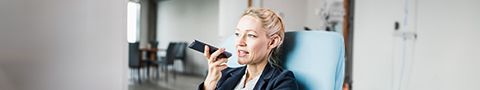 A person in professional attire sitting and talking on speaker on a smartphone. 