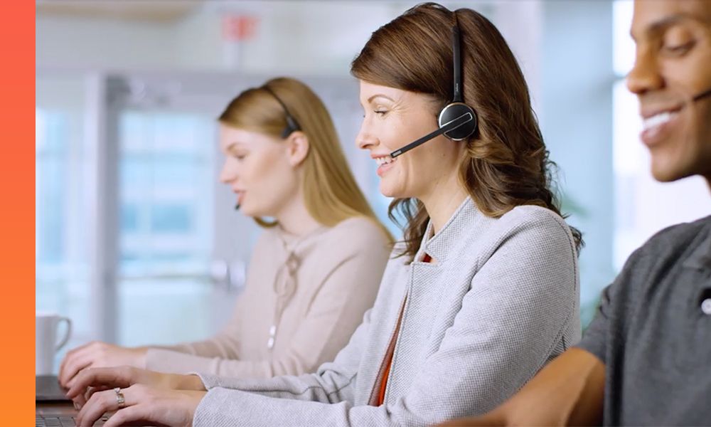 Three people wearing headsets talking and working at computers.