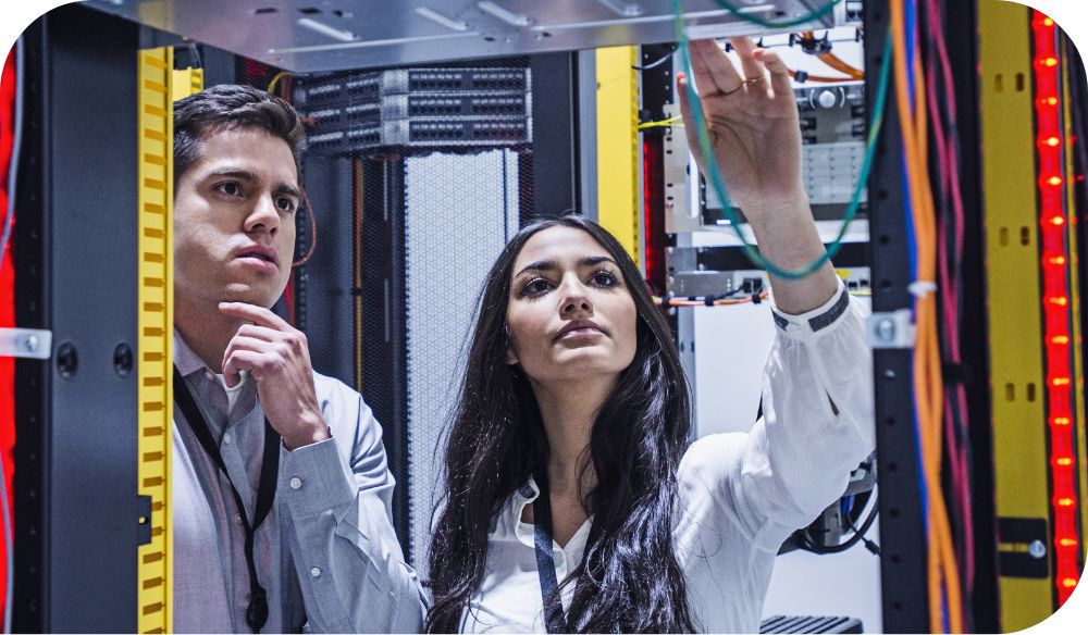 Two people examine wires in a server room