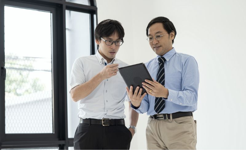 Two men in business attire study a tablet in a brightly lit office