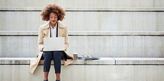 Woman sitting outside on a stone step while working on a laptop
