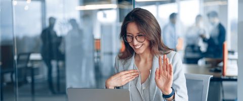 Businessperson sits in front of a laptop screen while smiling and making hand motions