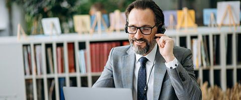 A man in a suit works on a laptop and talks on a headset