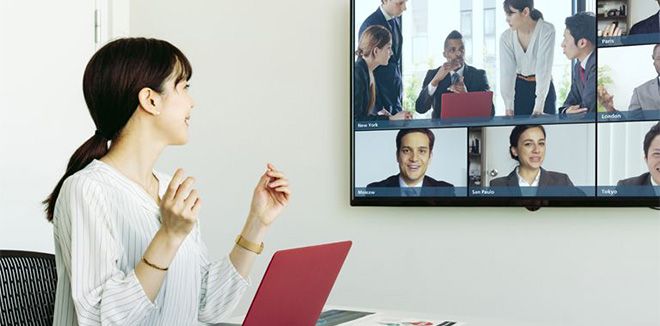 Women sitting in a conference room looking at a TV with a conference call showing 6 people