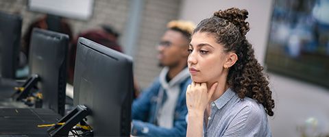 Students in a classroom view course content on monitors
