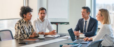 Four people sitting at a conference table while talking and working with papers and laptop devices in front of them