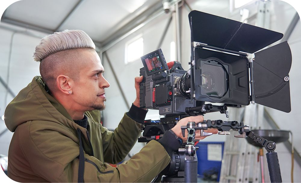  A person with a mohawk hairstyle operates a video camera mounted on a tripod