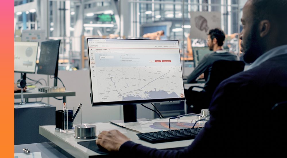 IT professional viewing networking map on computer monitor sitting at desk inside operations center.