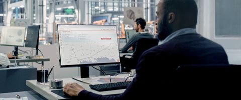 IT professional viewing networking map on computer monitor sitting at desk inside operations center.