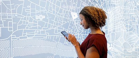 A person reviews information on a smart phone while standing in front of a digital map.