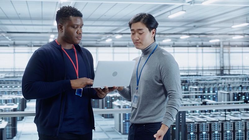 Two people in a data center look at a laptop together.