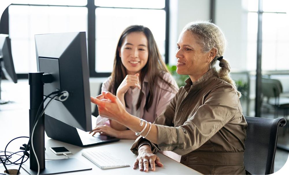 Two people discuss information shown on a desktop computer in an office. 