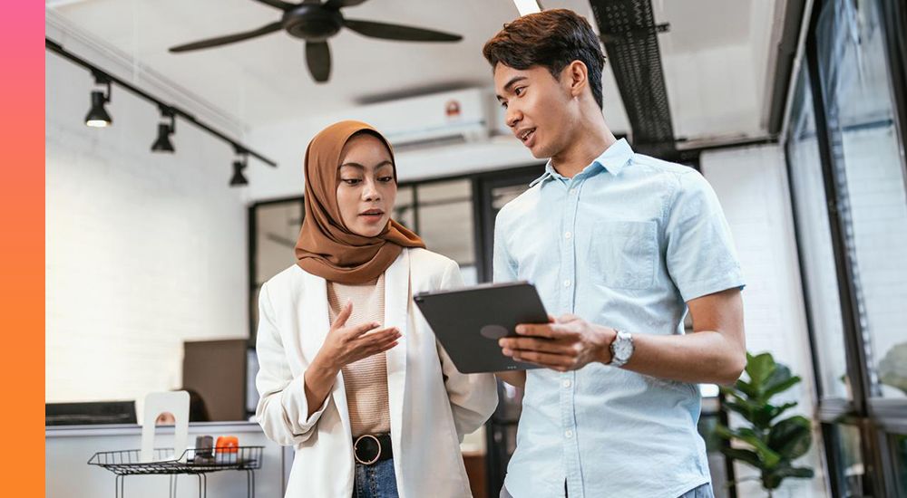 Two people walk together while discussing information shown on a tablet. 