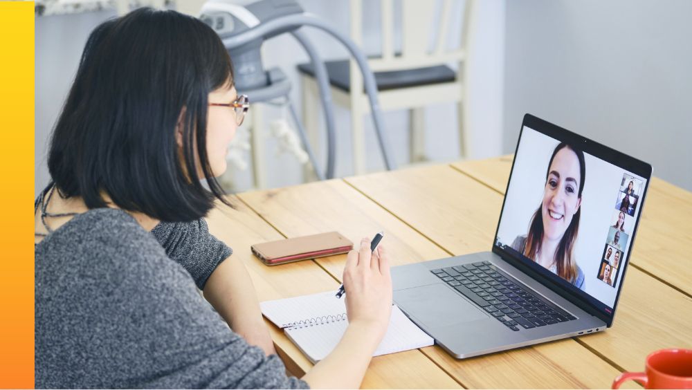 A person sitting at a table in front of a laptop participating in a Webex video meeting