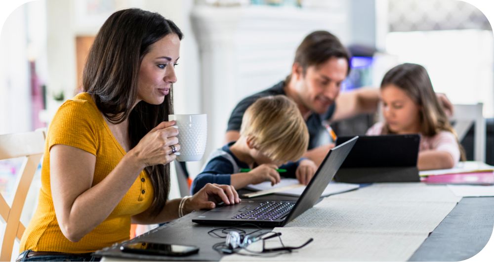 Mother and father working at table with son and daughter reviewing content on their laptops. 