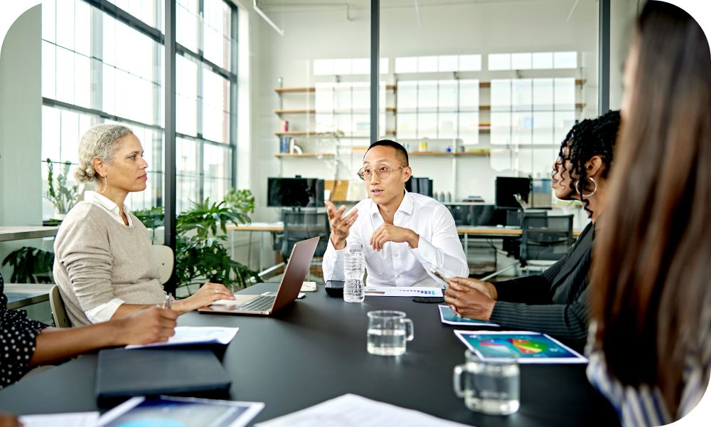 Man in a white shirt sitting at the head of a conference table while talking to four other people