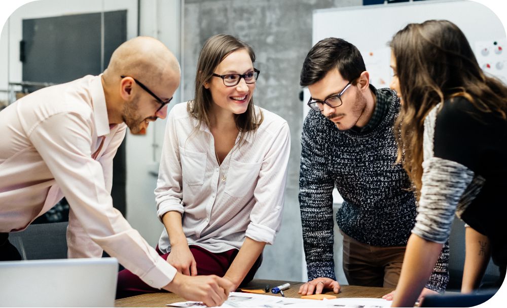 A group of professionals stands around a conference table reviewing and discussing documents on the table