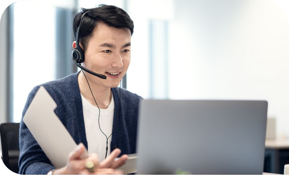 A person wearing a headset sits at a desk and works on a laptop