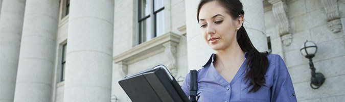 Business woman standing outside of a building while looking at a tablet device