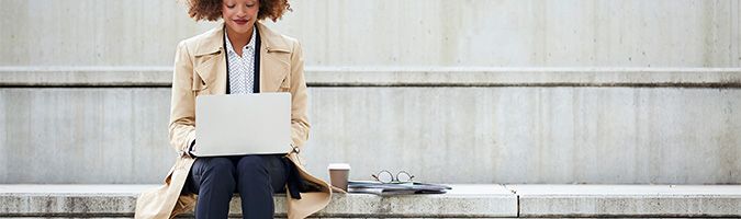 Woman sitting outside on a stone step while working on a laptop